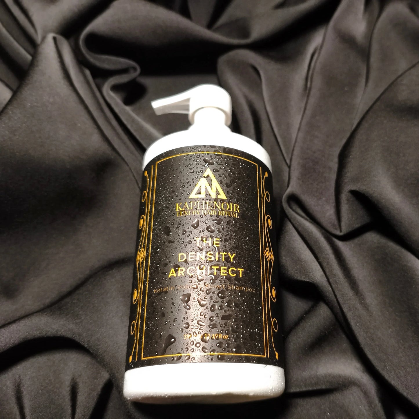 KapheNoir black and gold bottle labeled 'The Density Architect' on black fabric